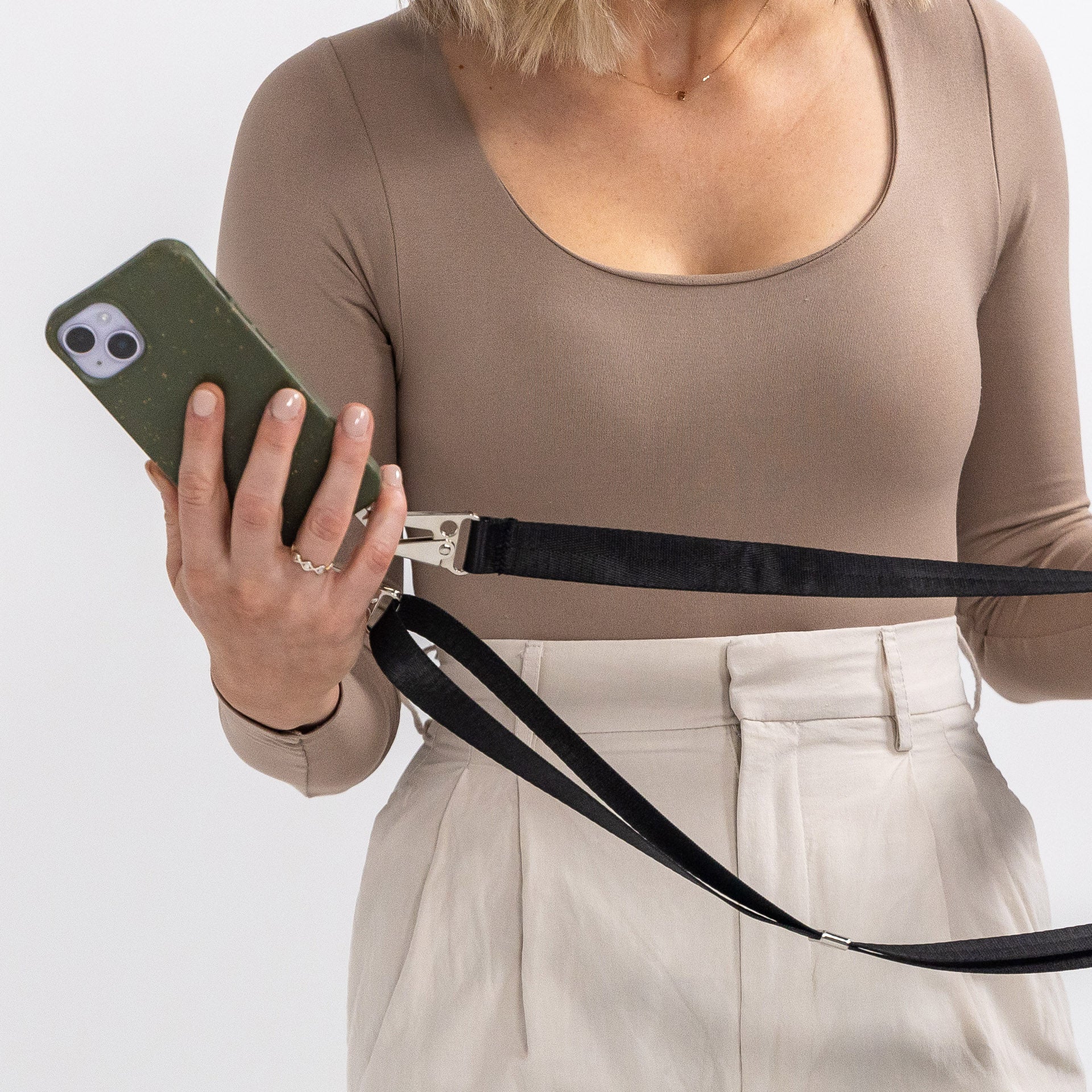 Pesto crossbody phone case with black strap being held on the side in front of body