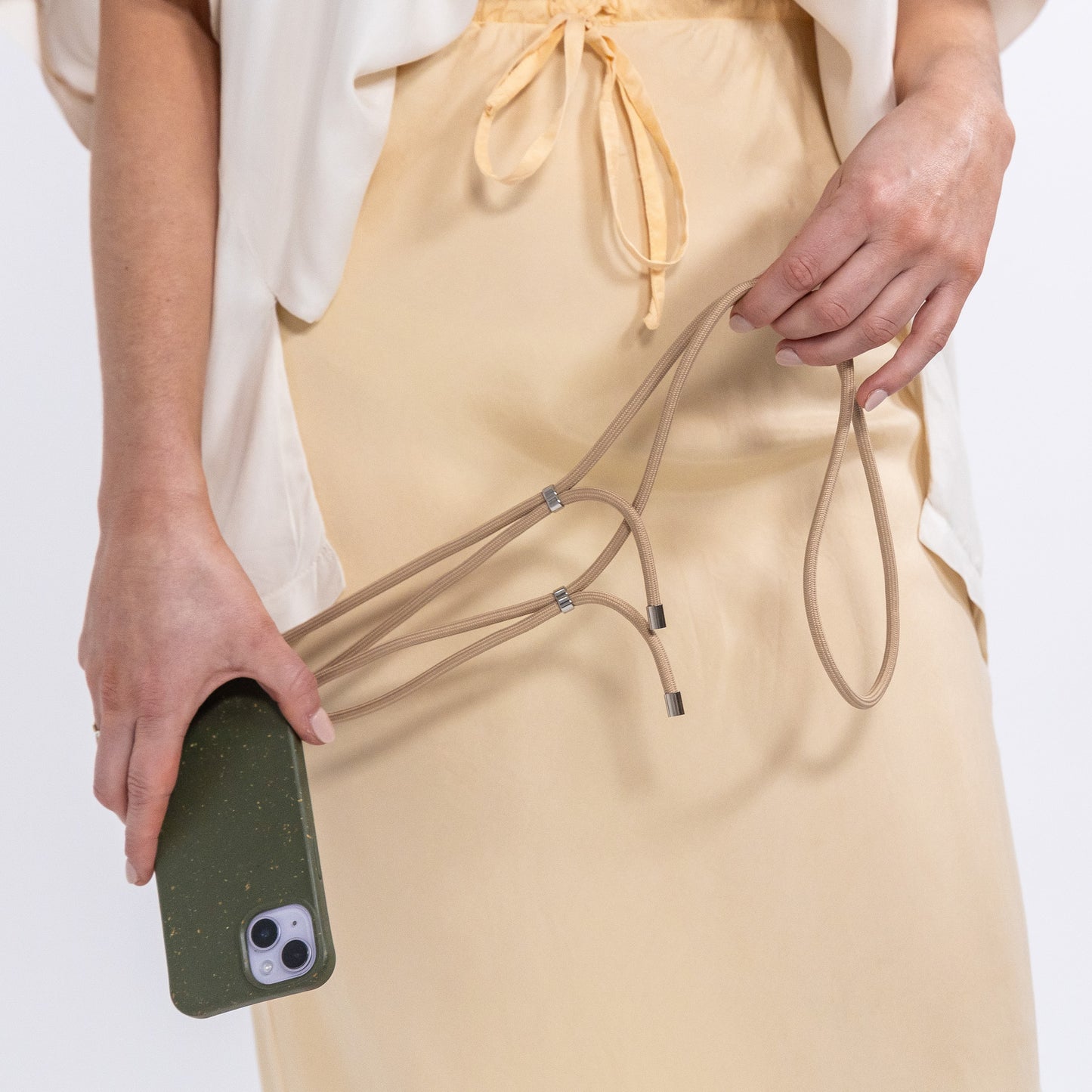 Pesto crossbody phone case being held in hand with tapioca cord attached