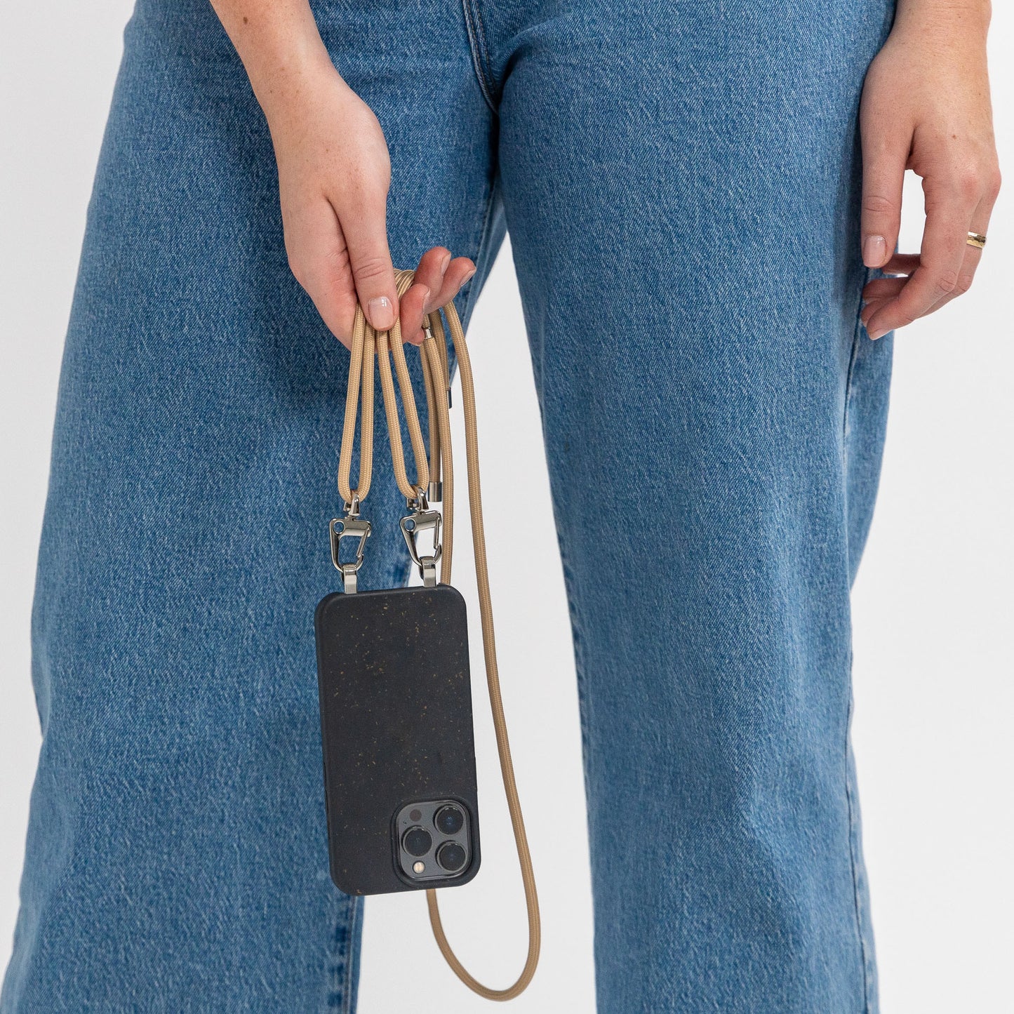 Ink crossbody phone case with tapioca cord attached being held in front of legs 