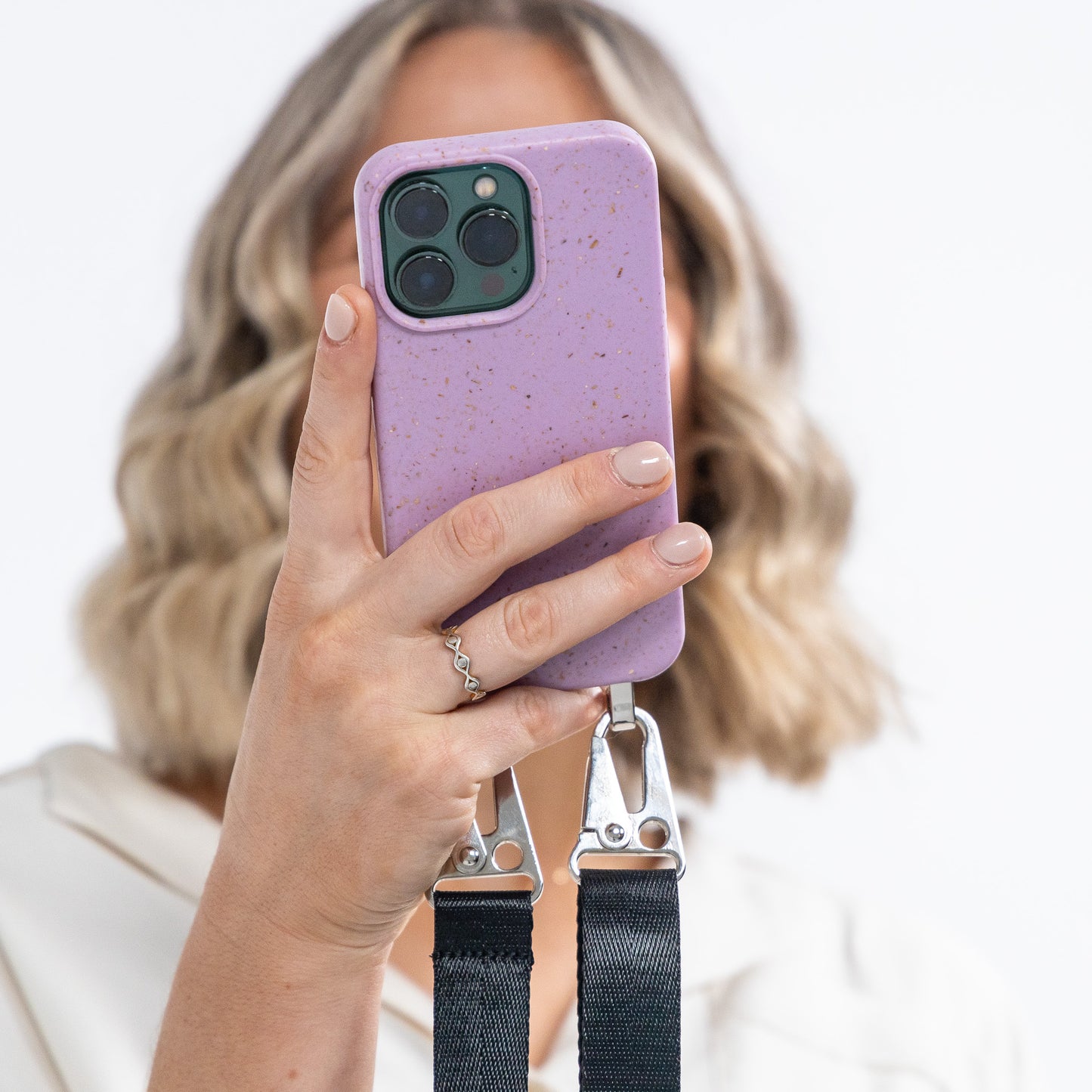 Lavender crossbody phone case being held in hand with black strap attached