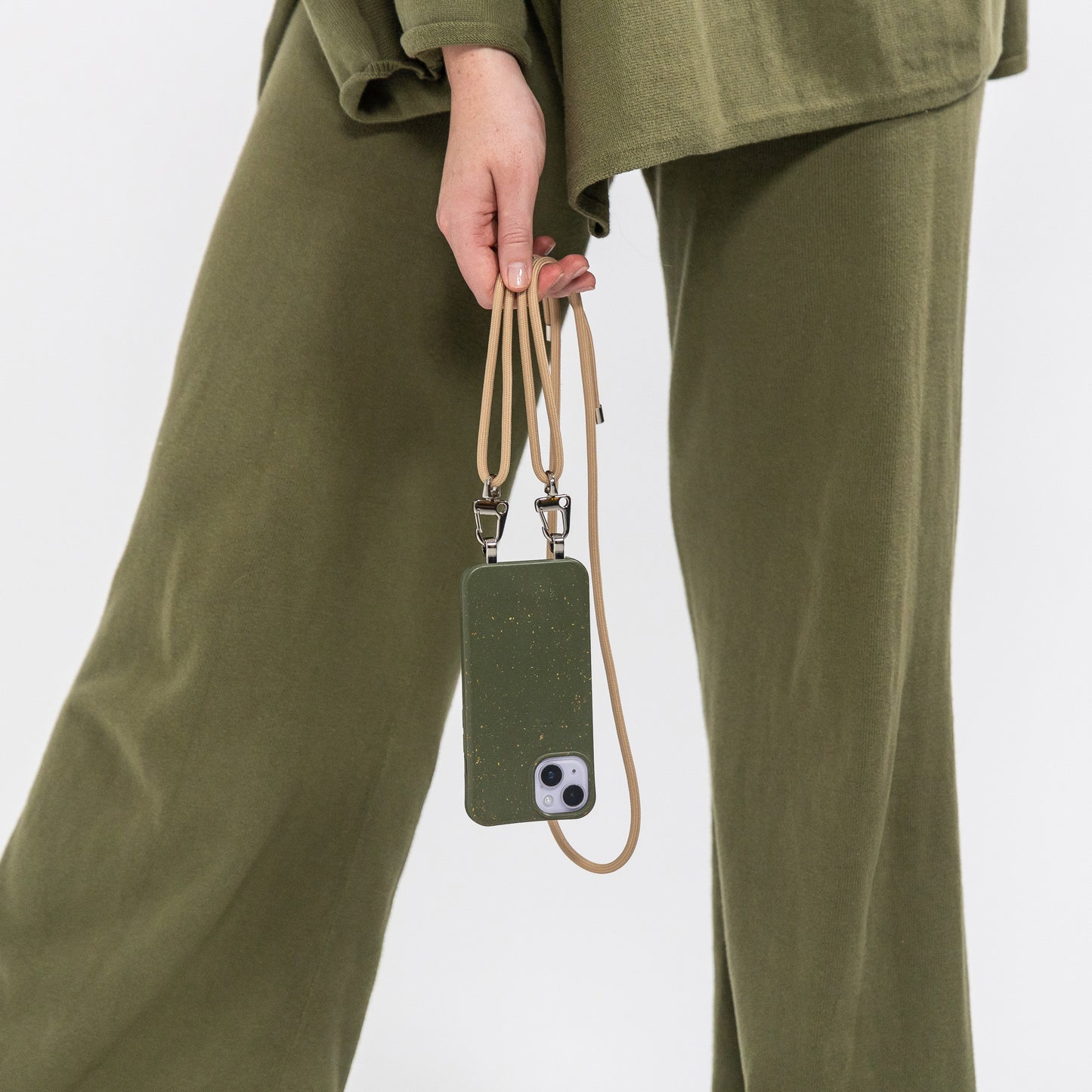 Pesto crossbody phone case with tapioca phone cord hanging and being held 