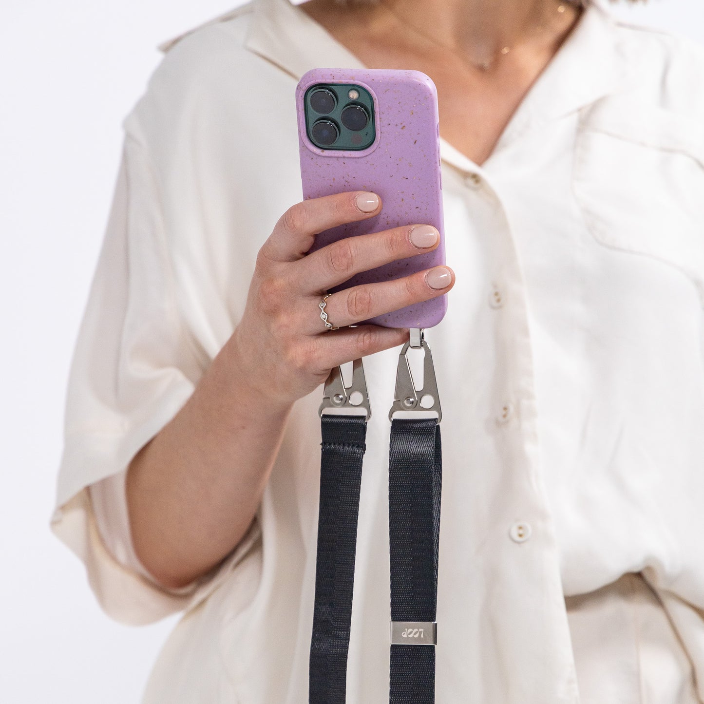 Lavender crossbody phone case with black strap being held with view from behind